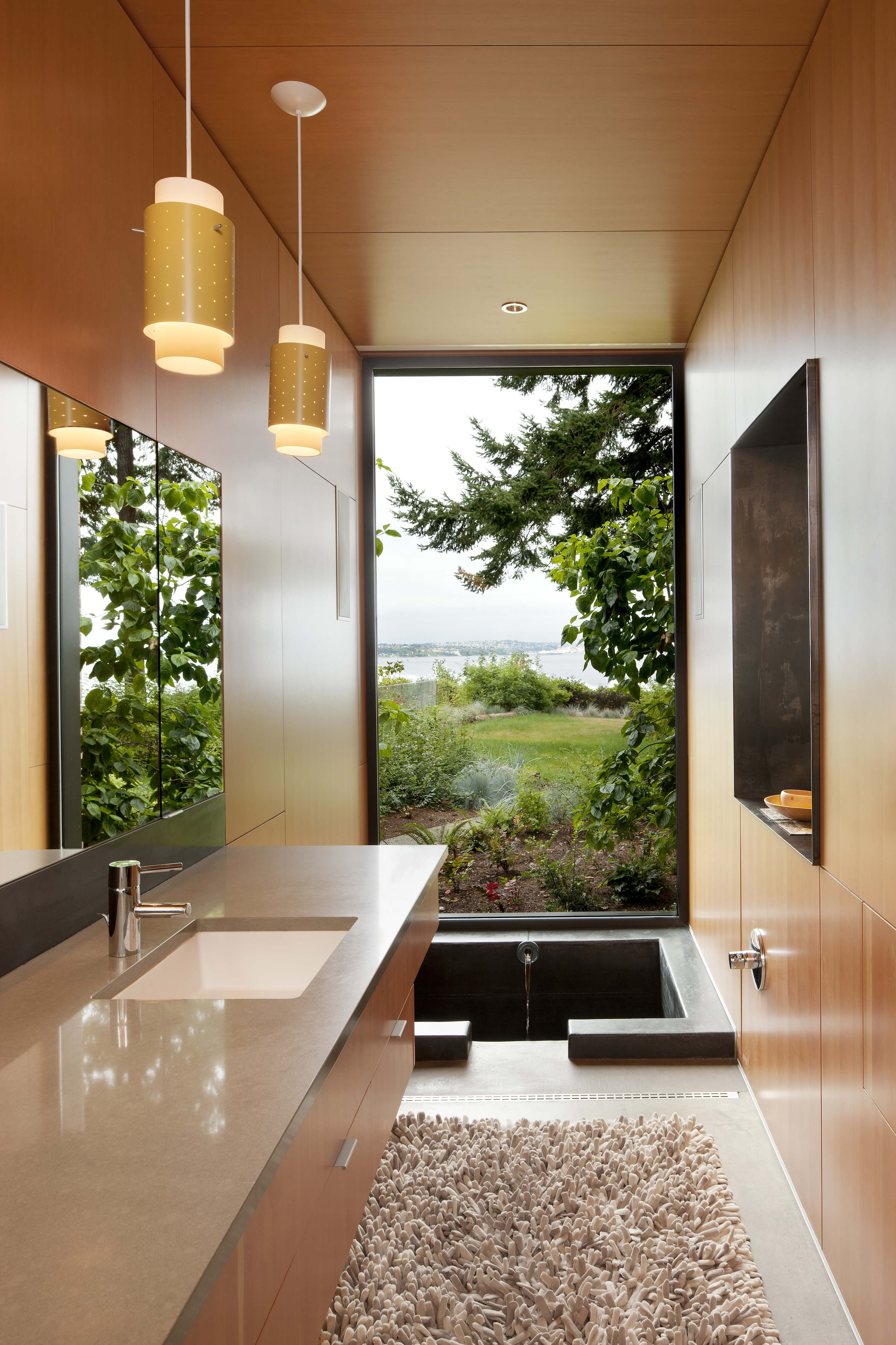 浴室具有完整的室外景观，地板上有凹陷的浴缸，墙壁和橱柜上有简约、光滑的木板。