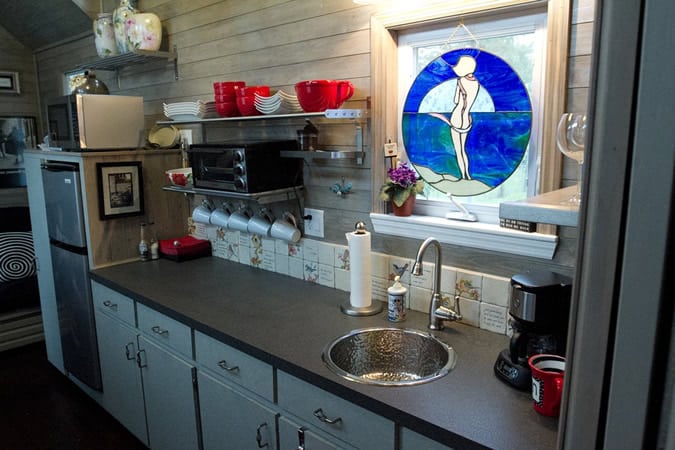 全功能的厨房拥有长长的黑色台面和水槽，在彩色玻璃罩下，电器在左侧。