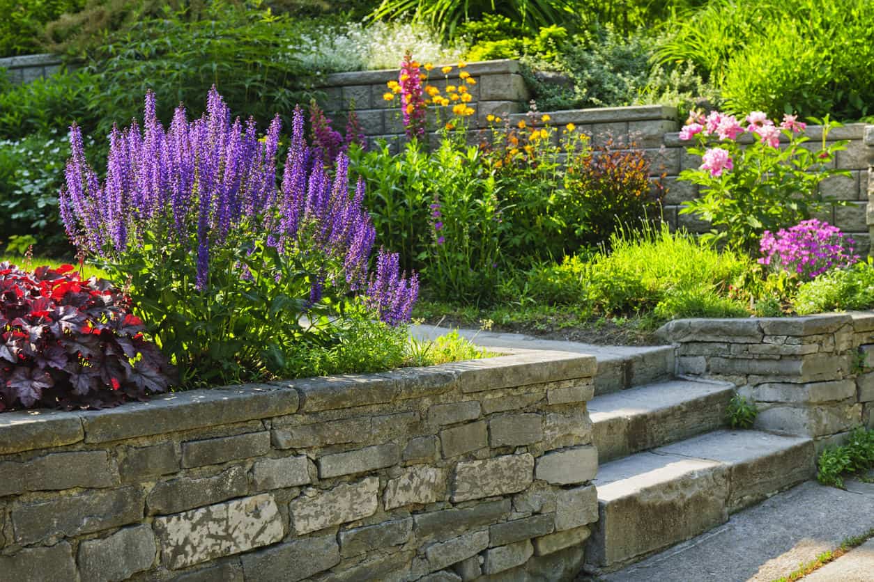 天然石材挡土墙环绕着宏伟的花园，花园里长满了可爱的开花植物。