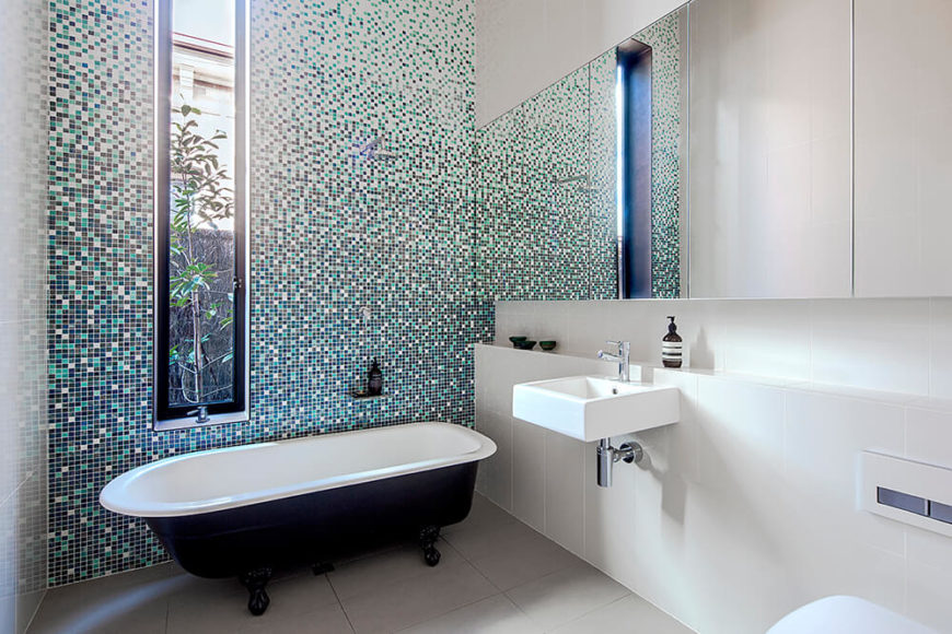 主浴室也以复杂的瓷砖墙为特色，这一次为白色空间提供了色彩。无框镜子和爪脚浴缸在这个现代空间中形成有趣的并列。