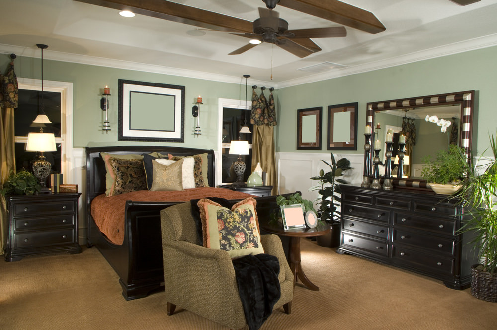 这间主卧室设有一张时尚的床，周围环绕着绿色的墙壁和白色的托盘天花板，以及棕色的地毯地板。
