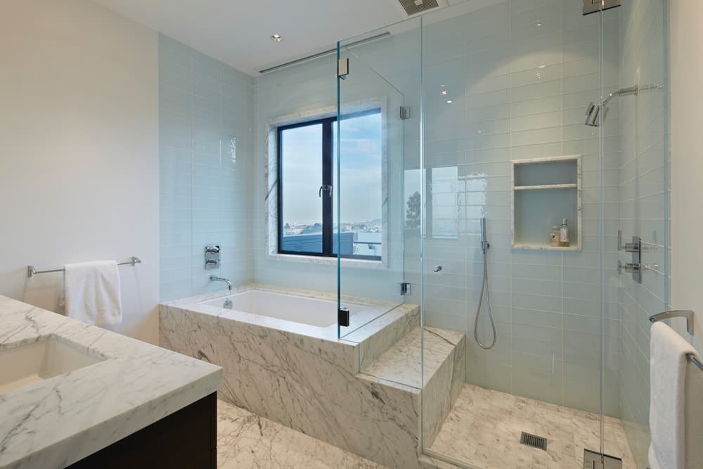 现代白色浴室，带浴缸和步入式淋浴，以及大理石台面和地板。图片来源:Bruce Damonte