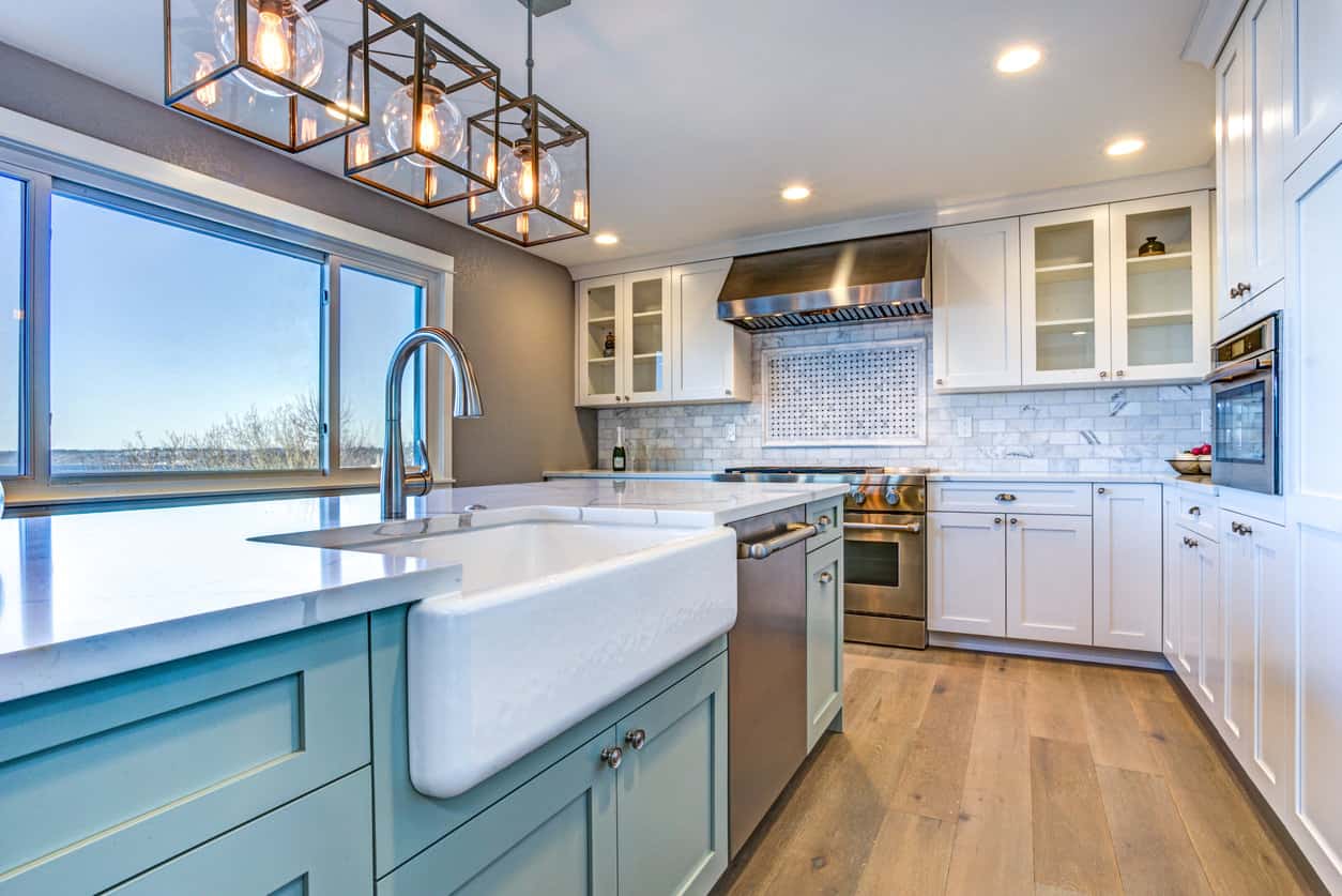 厨房配有蓝岛、大型白色农舍水槽、白色橱柜和宽木板硬木地板，所有这些都配有当代单体吊灯和嵌入式灯。