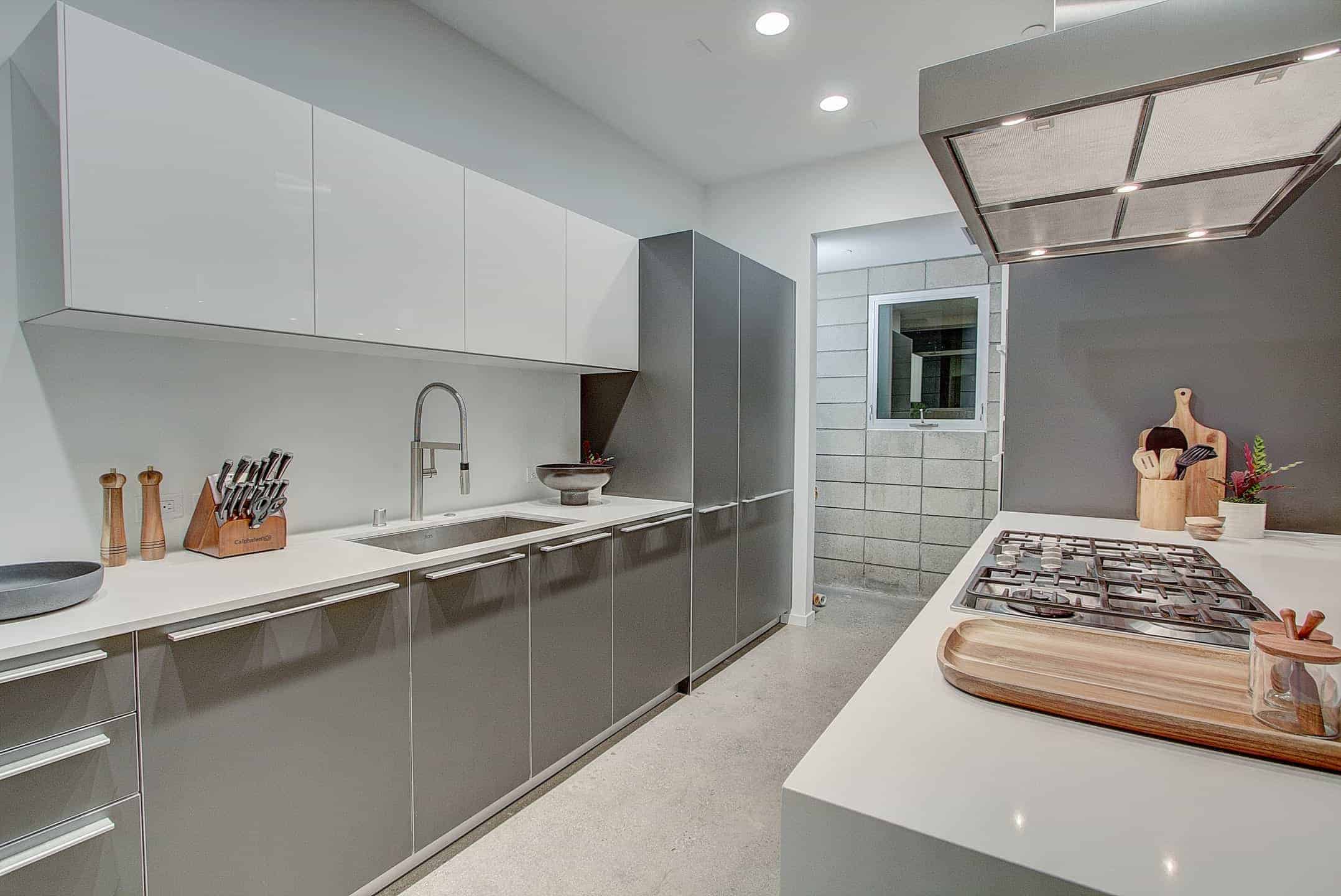 厨房设有灰色的厨房柜台和中央岛台，都有光滑的白色台面，并由嵌入式天花板灯照明。