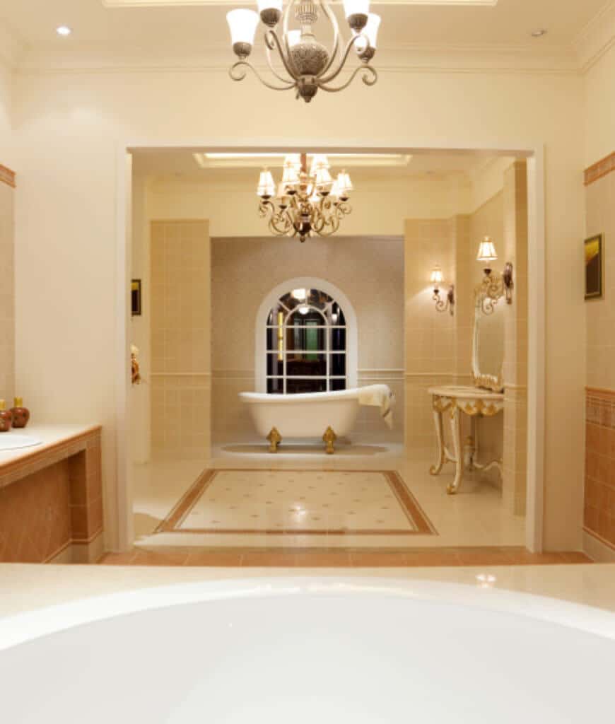 这间主浴室的特色是拱形窗户旁边有一个爪足浴缸，旁边还有一张优雅的白色桌子和一面镜子。