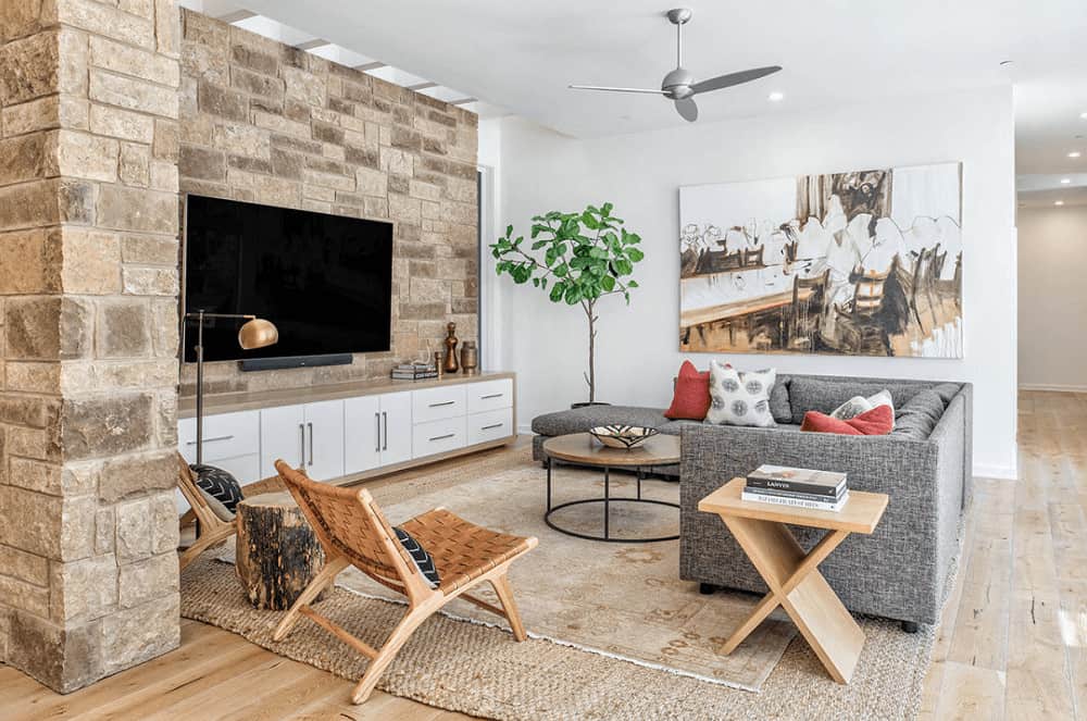 在这个新鲜的客厅里，一面镶有电视的石墙增加了质感，灰色沙发、柳条椅和木桌搭配在一起。它包括一个大型艺术品和铺在宽阔木板地板上的棕色分层地毯。
