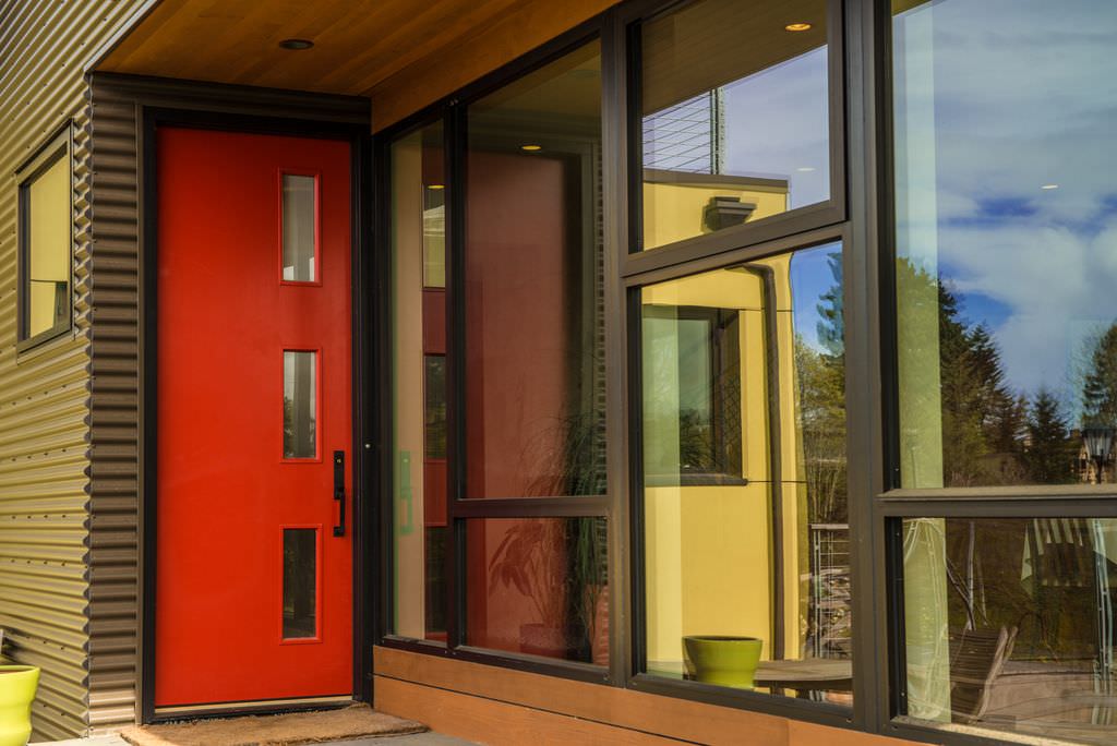 在这座现代住宅中，一扇带有玻璃镶嵌和锻铁把手的光滑的红色门格外显眼，它展示了灰色的壁板和玻璃镶板窗户。