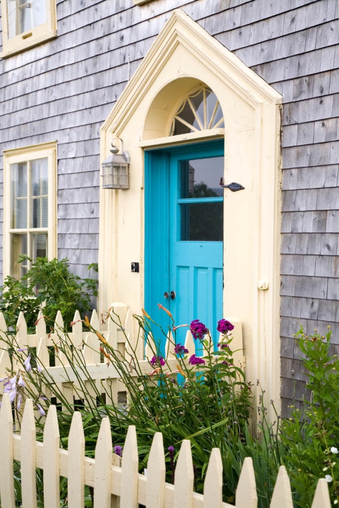 绿松石的前门为这座房子带来了一种流行的色彩，它覆盖着浅色的木壁板。它是由铬壁灯和围绕绿色植物的奶油色围栏补充。
