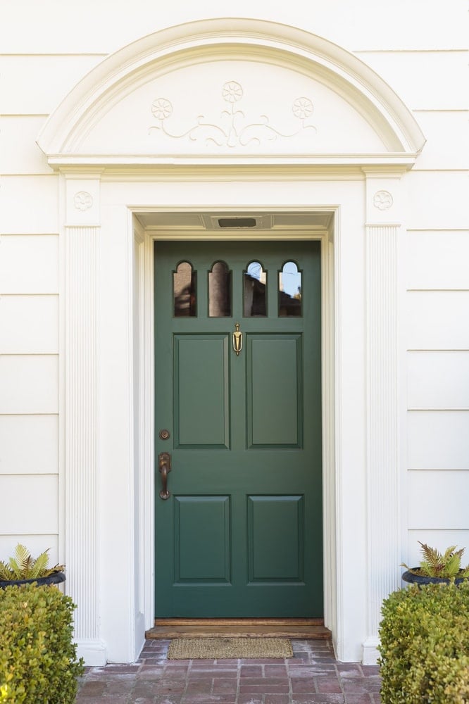 翡翠绿的门装有拱形玻璃嵌件，青铜把手和黄铜门环。它被白色的柱形装饰所包围，头顶上的拱形装饰设计有简单的花卉雕刻。