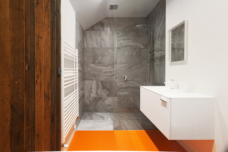 小型定制主浴室，配备橙色瓷砖地板和白色墙壁，以及浮动梳妆台水槽。还有一个步入式淋浴间，以灰色瓷砖地板和墙壁为特色。
