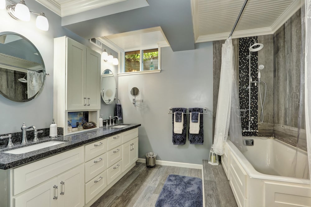 主浴室设有蓝灰色墙壁和硬木地板，侧面设有淋浴和浴缸组合，以及一个带花岗岩台面的水槽柜台。
