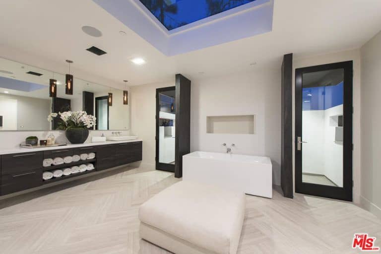 现代定制主浴室，具有时尚的地板和天窗天花板。房间里有一个独立的浴缸和一个带有嵌入式架子和橱柜的漂浮梳妆台。