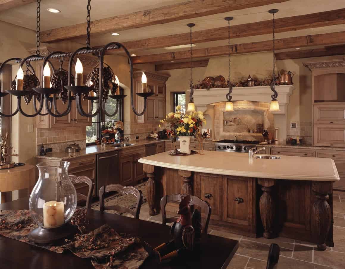 这是一个大而家庭式的地中海式厨房，厨房岛上有配套的木制橱柜和抽屉，墙壁上有L形橱柜。这些与天花板上裸露的木梁相匹配，天花板上悬挂着一行锻铁吊灯。