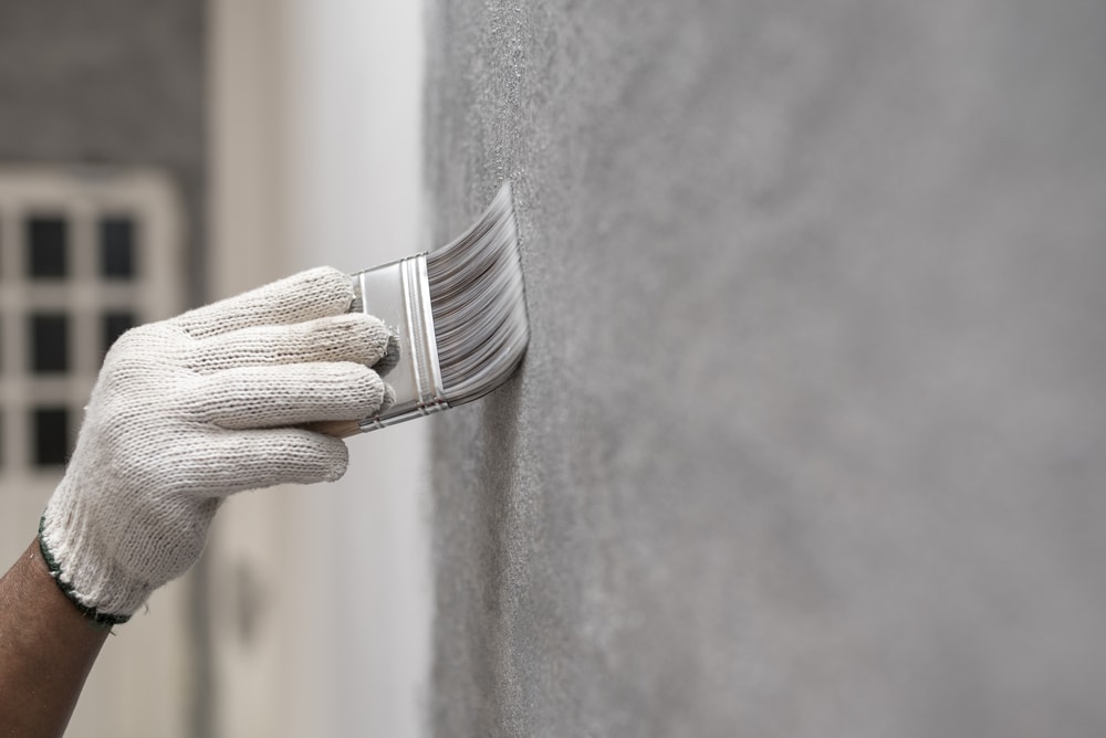这是一只戴着手套的手用平漆覆盖墙壁的近景。
