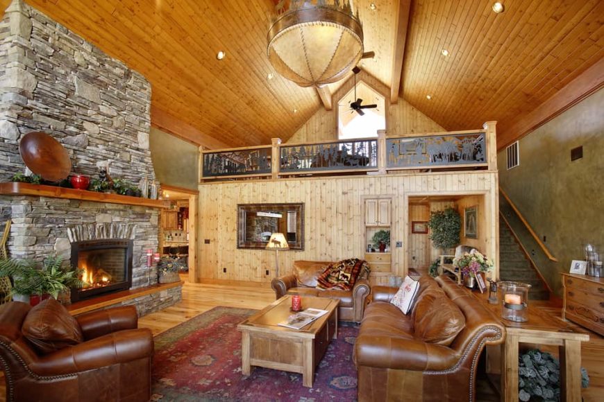 从这里可以看到这座山小屋风格的客厅的全貌，这里有高高的木制教堂天花板、棕色皮革沙发和木制咖啡桌对面的一座大型马赛克石壁炉。