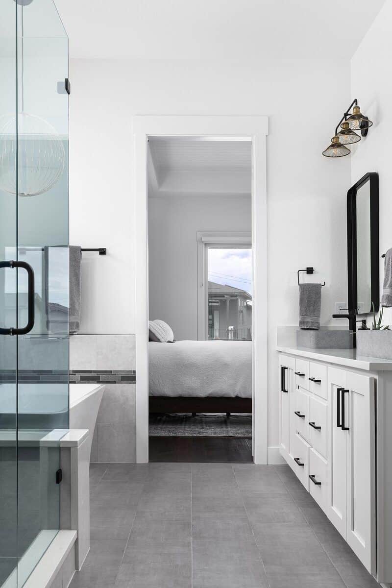 主浴室里有一间步入式淋浴间、一间独立式浴缸和一座白色梳妆台，配有双容器水槽和铁框镜子。