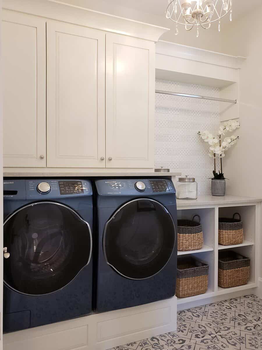 洗衣房有前置电器、白色橱柜和装满柳条篮子的储物架。