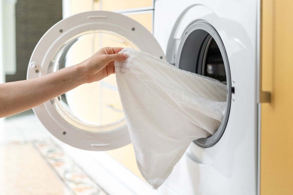一位女士从现代洗衣机中取出一条白色干净毛巾的裁剪图像。