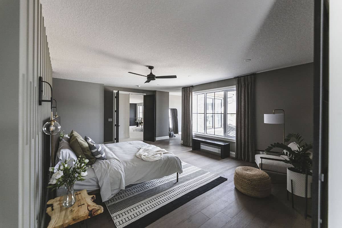 主卧室有一张舒适的床，条纹地毯，软垫躺椅，靠窗的木凳。