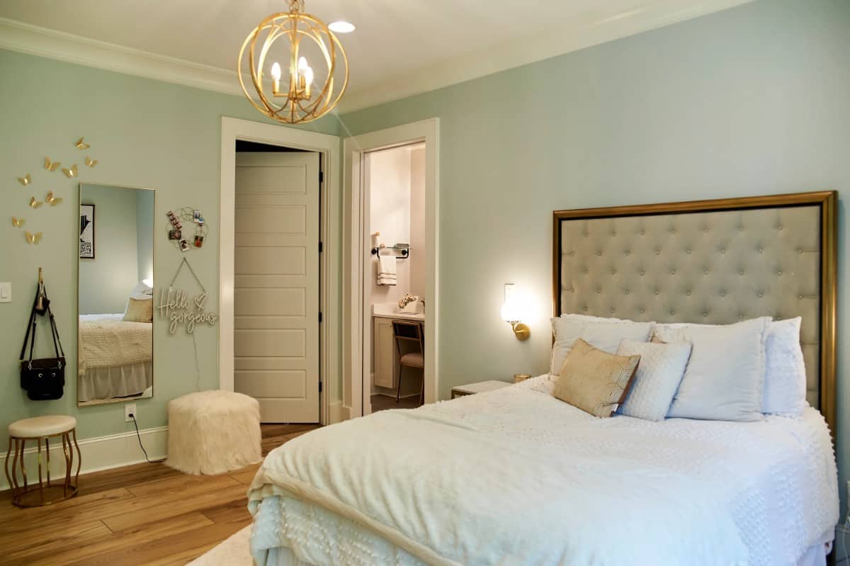 这间卧室有一张簇绒床、一盏球形吊灯和一面带凳子的长镜。